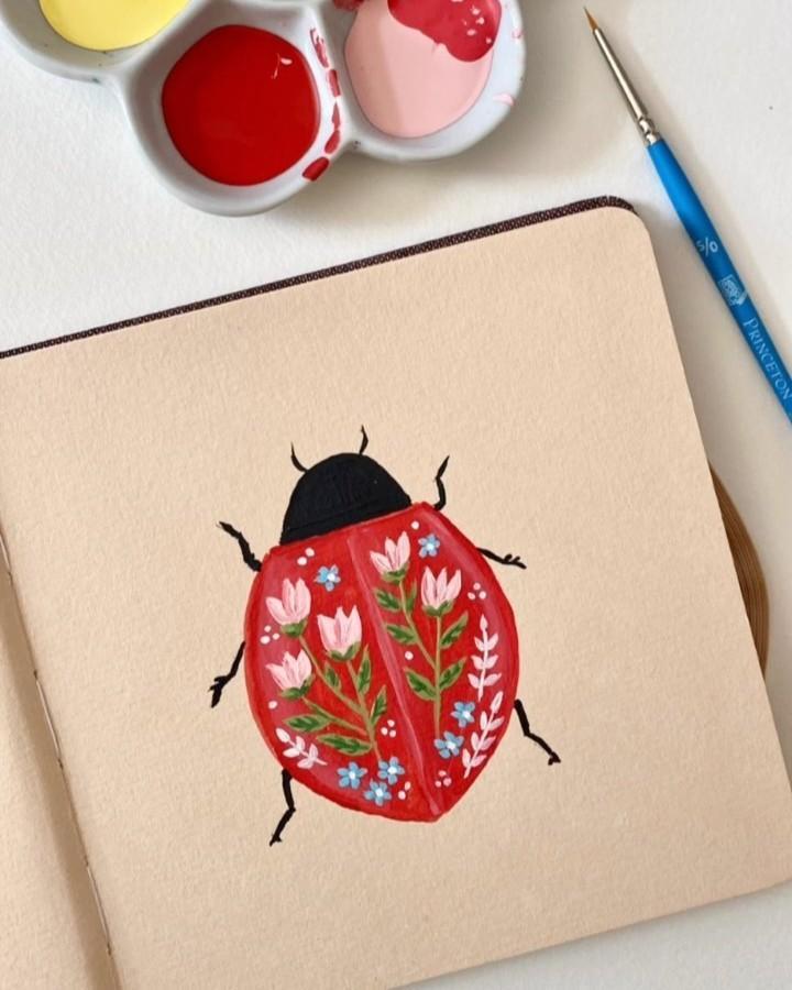 Red ladybug painting with floral patterns on cream paper using acrylics and a fine brush from @alexandrasillos. Intricate ladybug crafts for adults.