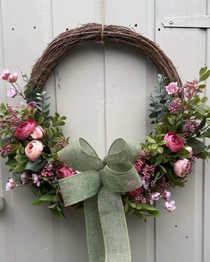 Natural grapevine wreath decorated with pink flowers and green leaves from @giftful_handmadecrafts featuring spring wreath ideas and a soft green bow.