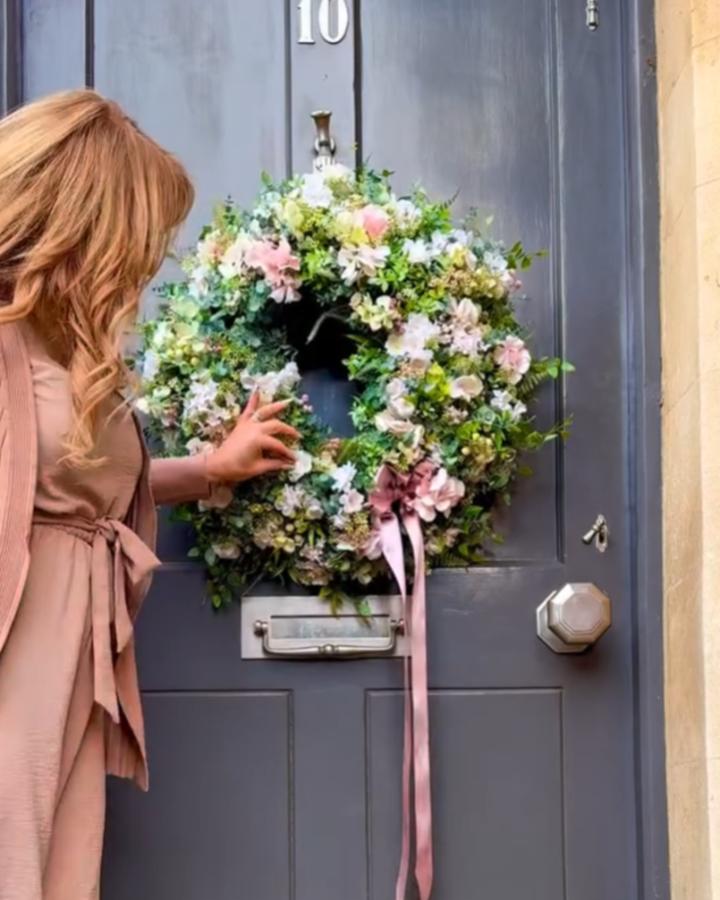 lush pastel floral spring wreath ideas on blue door with trailing pink ribbon from @whispering.lily woman touching flowers