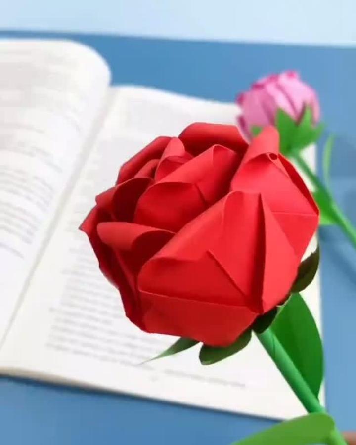 Red and green origami rose valentines crafts for adults from @littlemiisscraftss with detailed folded petals and leaves on a blue background.