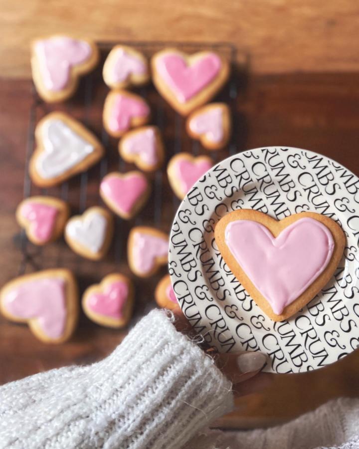 Pink and white iced heart cookies from @amber.adey for valentines crafts for adults held over patterned plate.