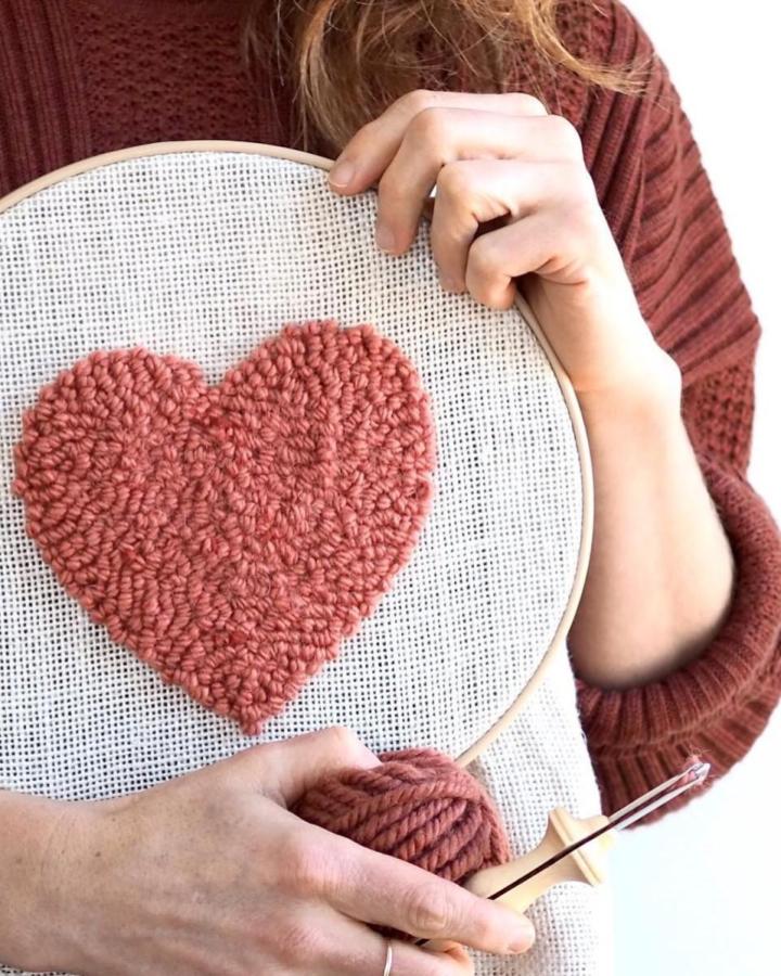 Thick dusty rose yarn punch needle heart valentines crafts for adults from @rosepearlman held close by woman in rust sweater