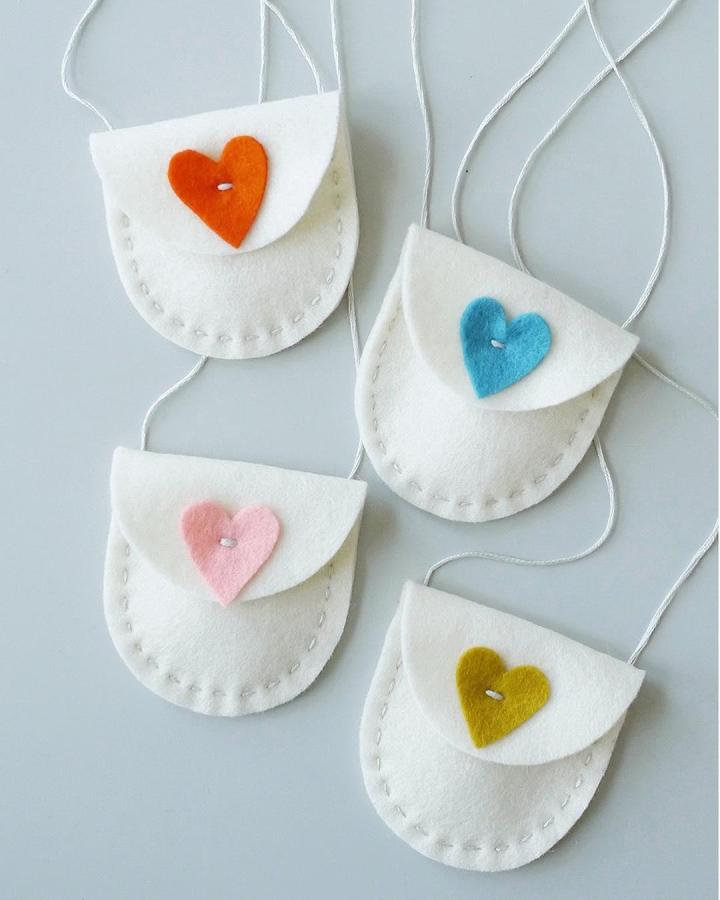 White felt mini purses with colorful heart closures in orange, blue, pink, and mustard from @fairplayprojects valentines crafts for kids. Small sewn felt bags with string.