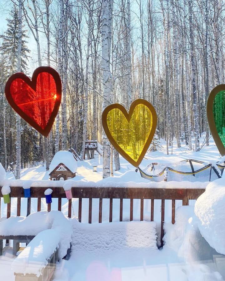 Bright red yellow and green stained glass heart crafts hanging on snowy window from @creativeandbusysquirrels. Valentines crafts for kids catching sunlight and brightening a winter view.