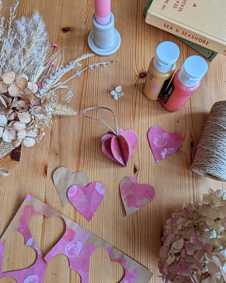 pink and gold painted paper hearts and twine on wooden table for valentines crafts for kids from @kirstiecrafts simple handmade decorations