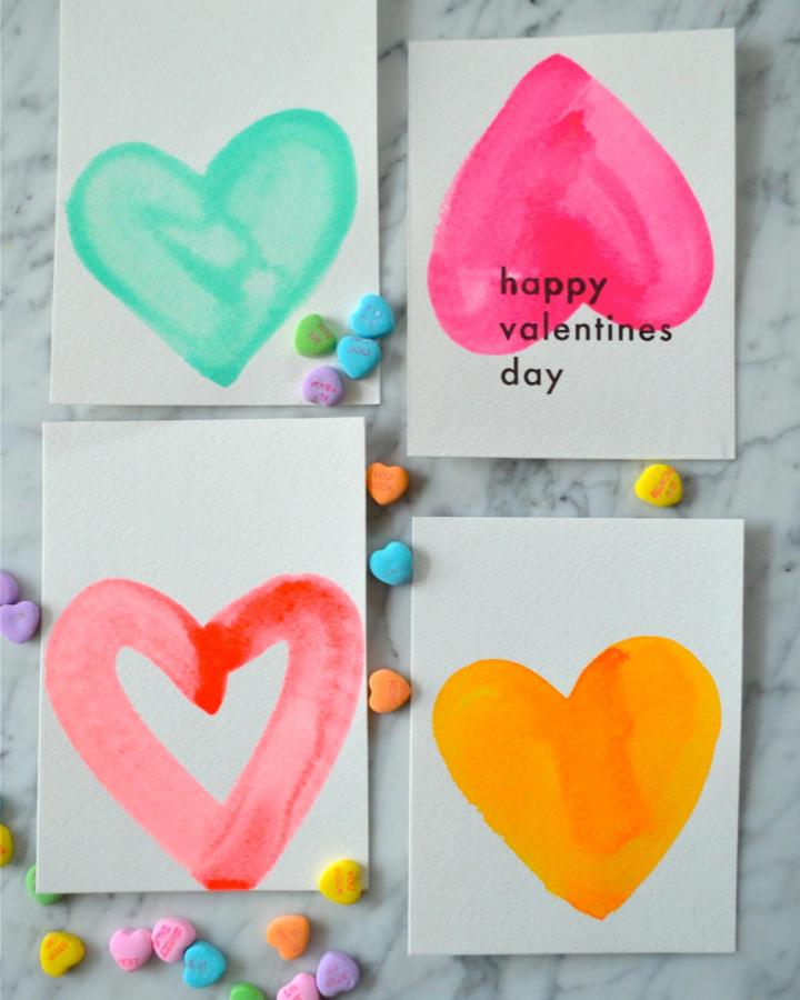Bright watercolor hearts on thick paper from Super Make It. Valentines crafts for kids with candy hearts scattered around.
