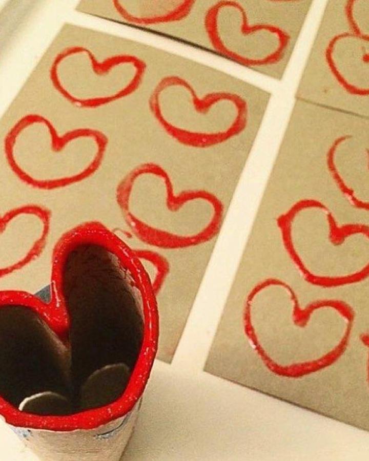 Red painted heart-shaped stamp craft from @naturallycuriouschildren showing valentines crafts for kids with brown paper background and red heart prints.