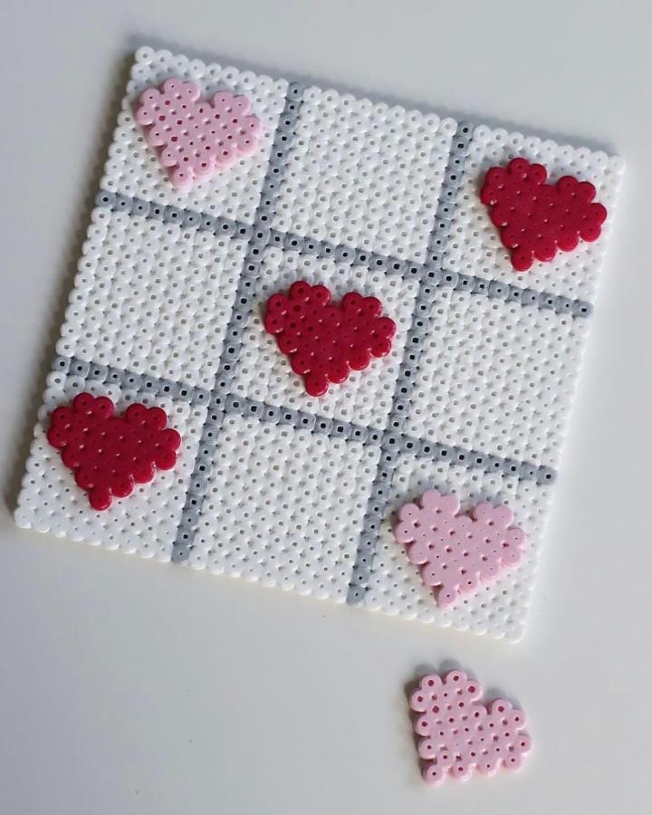 White and gray bead tic tac toe board with pink and red heart game pieces from @familjeprojektet Valentines crafts for kids. Cute, handmade heart shapes on a beaded grid.