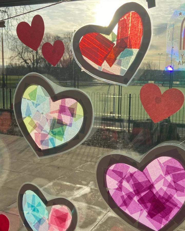Red and multicolored tissue paper stained glass hearts on window celebrating valentines crafts for kids from @kellylouise398. Bright and translucent heart shapes catching sunlight.