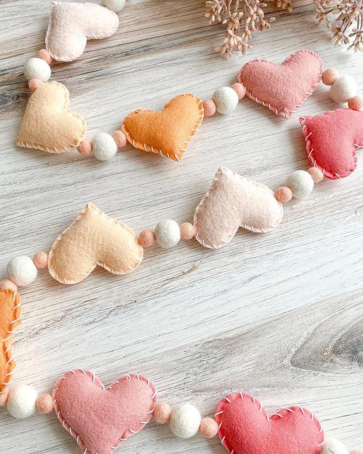 Soft pastel felt hearts and wool ball garland from @the.turquoise.leaf valentines heart garland ideas with cozy whipstitch detail