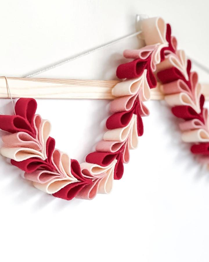 Soft red and pink felt hearts garland craft from @fern.and.love hanging on wooden dowel valentines heart garland ideas