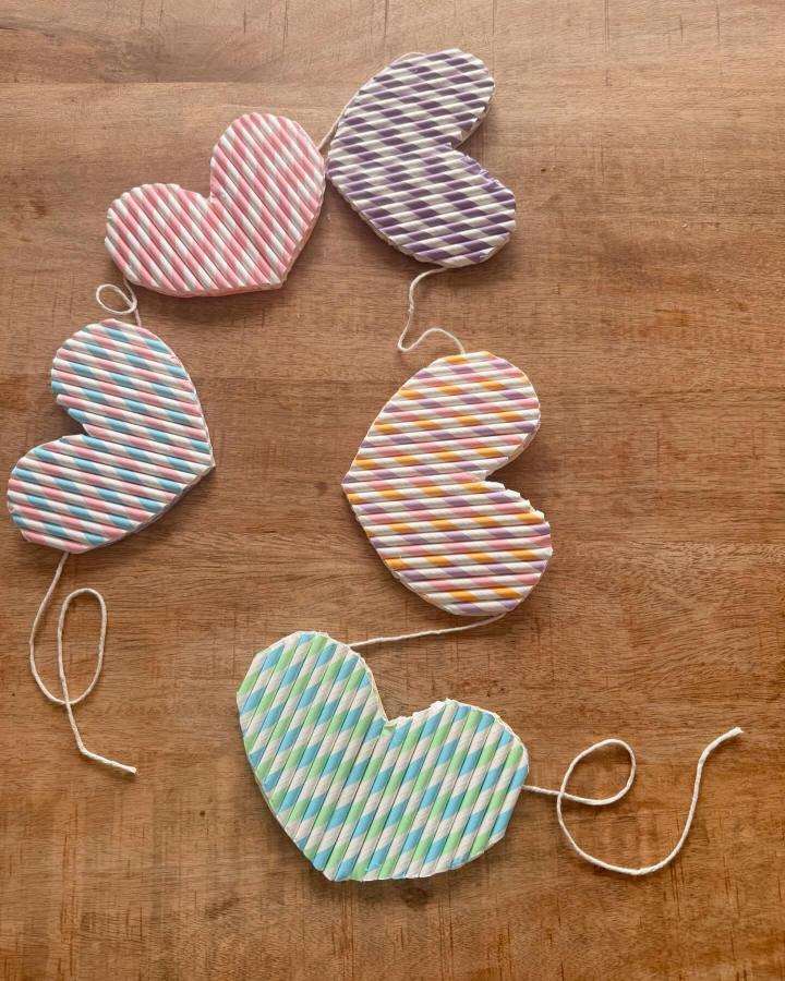 Pastel striped paper straw hearts garland from @littlecreativemakers with colorful Valentines heart garland ideas on wooden surface.