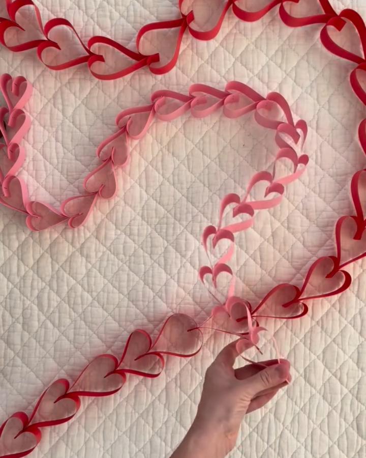 Red and pink heart-shaped paper chains from @leahfayegaeddert valentines paper craft ideas with a hand holding the chain on a quilted white background