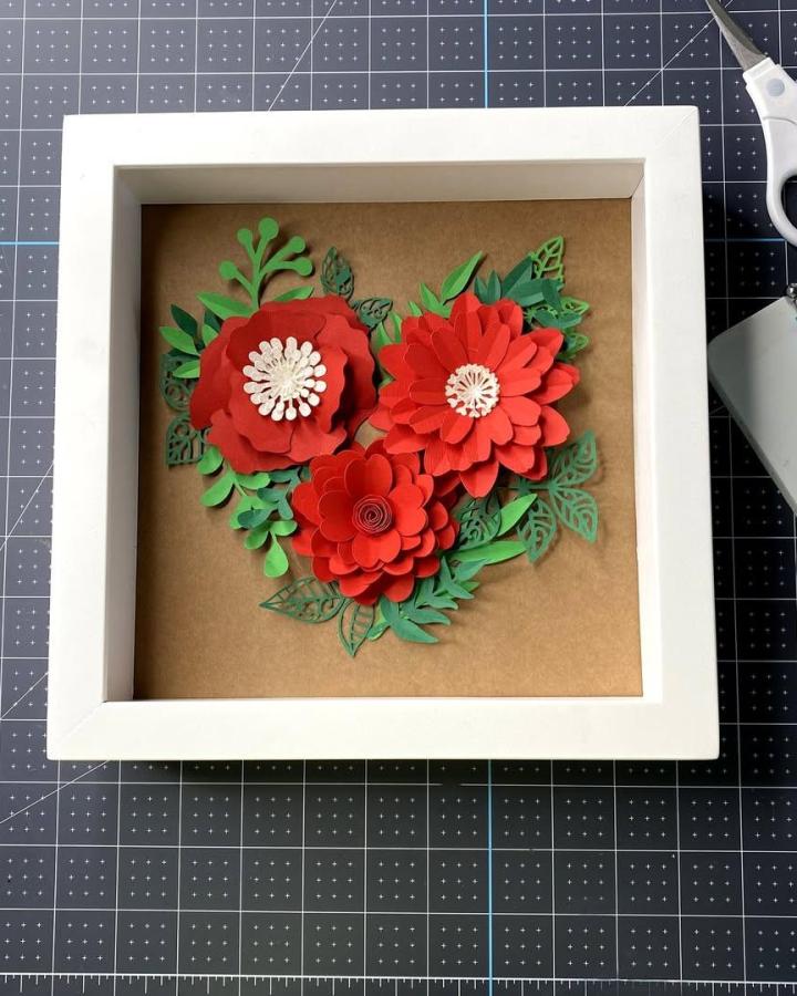 Red layered paper flowers and green leaves in a heart shape inside a white frame from @creative_vector_studio valentines paper craft ideas.