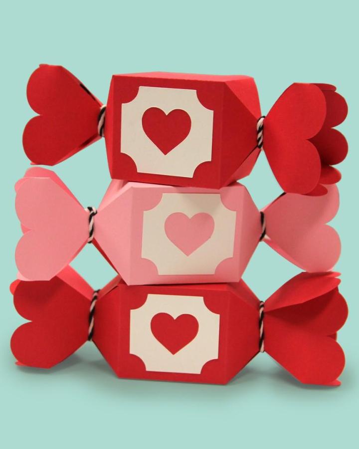 Red and pink heart-shaped paper candy boxes tied with twine from @printworksdiy for valentines paper craft ideas.