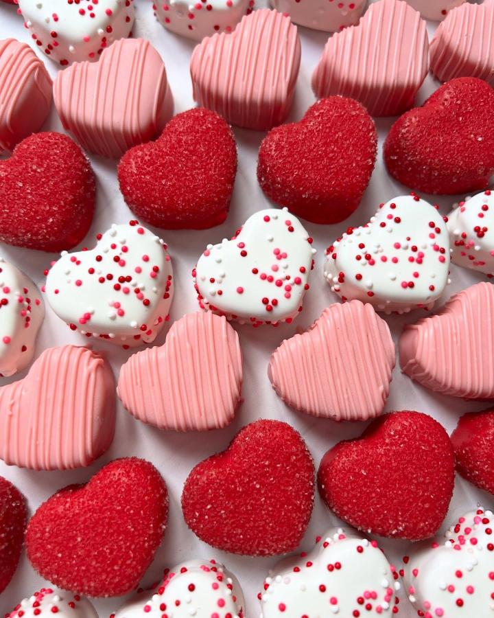 Red sugar-coated and pink and white chocolate-covered heart treats from @cakepopsbyrachel arranged in rows for valentines treat ideas.