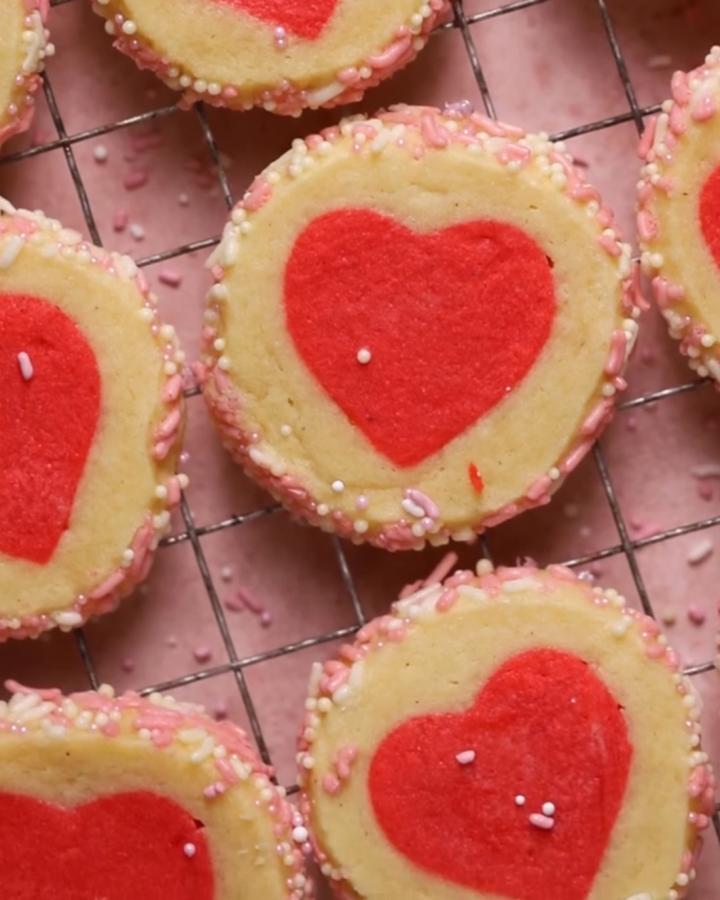 light beige and red heart cookies with pink and white sprinkles from @cambreabakes valentines treat ideas on cooling rack
