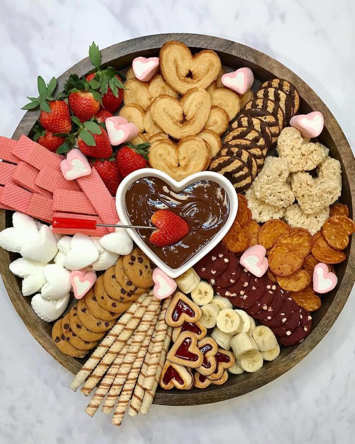 Pink heart-shaped cookies and assorted dipped snacks in a wooden platter from @thebakermama perfect for valentines treat ideas.