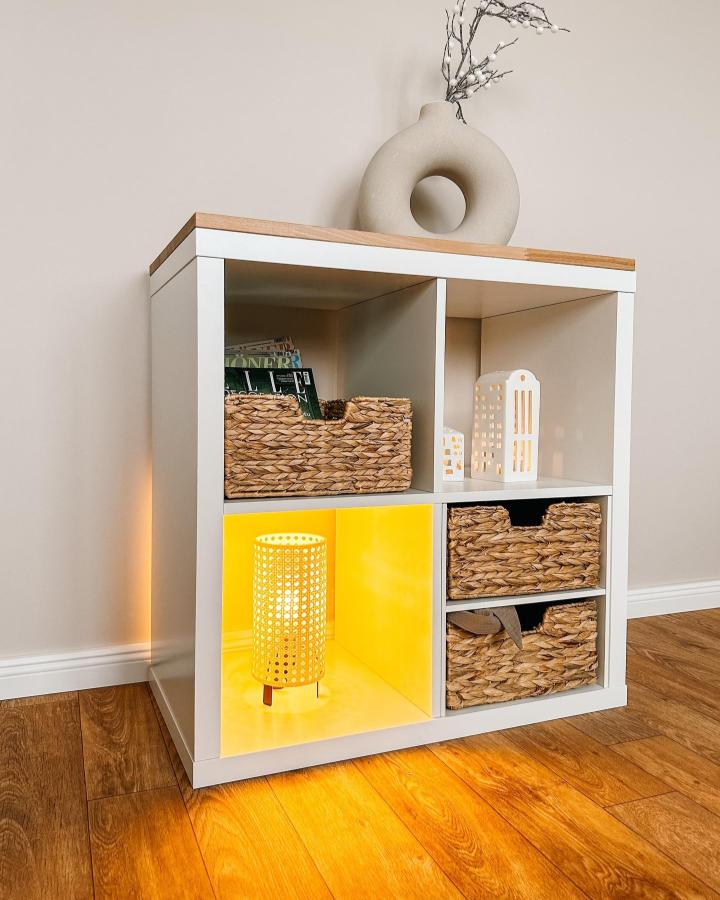 white and wooden ikea kallax inserts unit with woven baskets and yellow lamp lighting from @kallaxshop.de. Cosy stylish storage and mood lighting combination