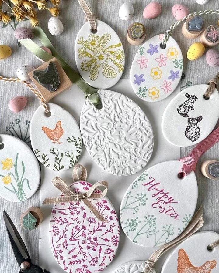 White oval clay tags with hand-stamped floral and animal designs by @my100yearoldhome. Easter clay craft ideas with ribbons and texture.