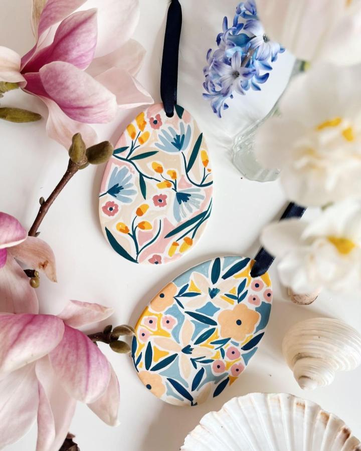 Light pastel floral patterned clay egg dish from @homebynela surrounded by spring flowers and seashells for easter clay craft ideas.