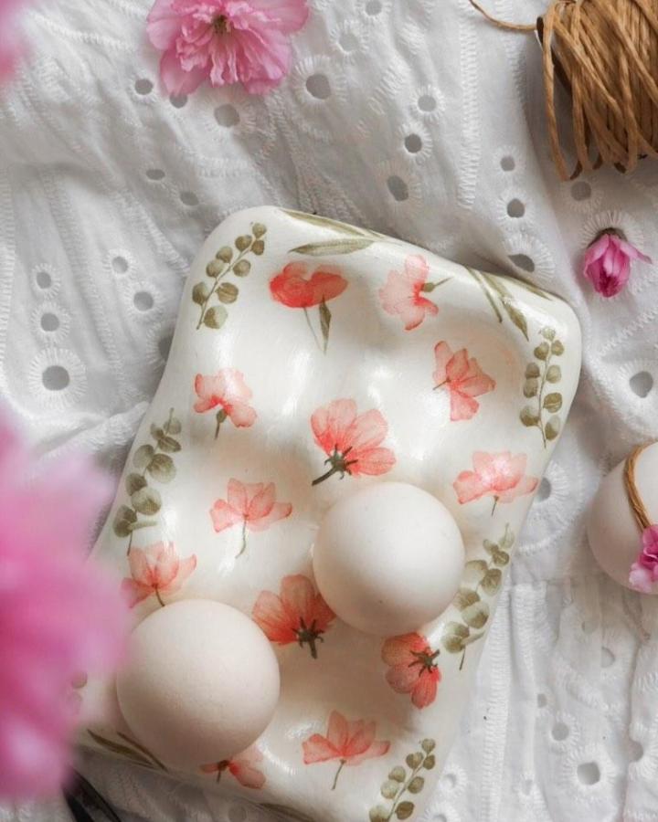 White hand-painted floral clay egg holder from @becki_clark_ with coral flowers and olive-green leaves for easter clay craft ideas.