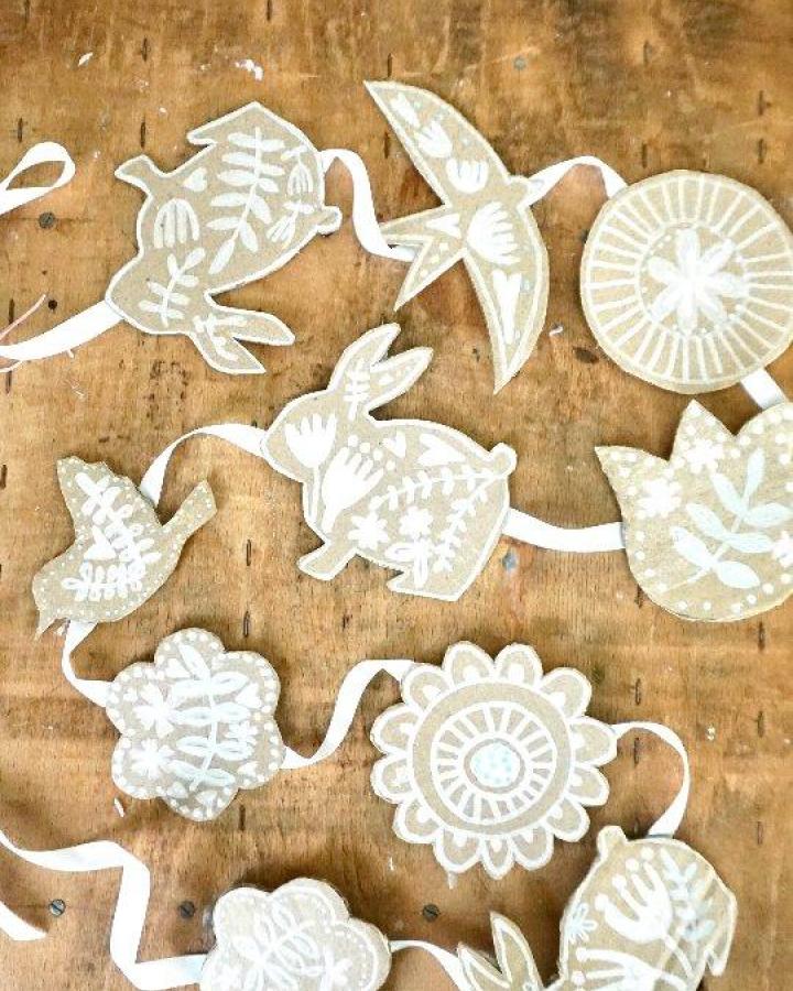 Natural kraft paper garland with white folk art designs from @caroline_crafts_at_home perfect for easter craft night ideas on wooden surface