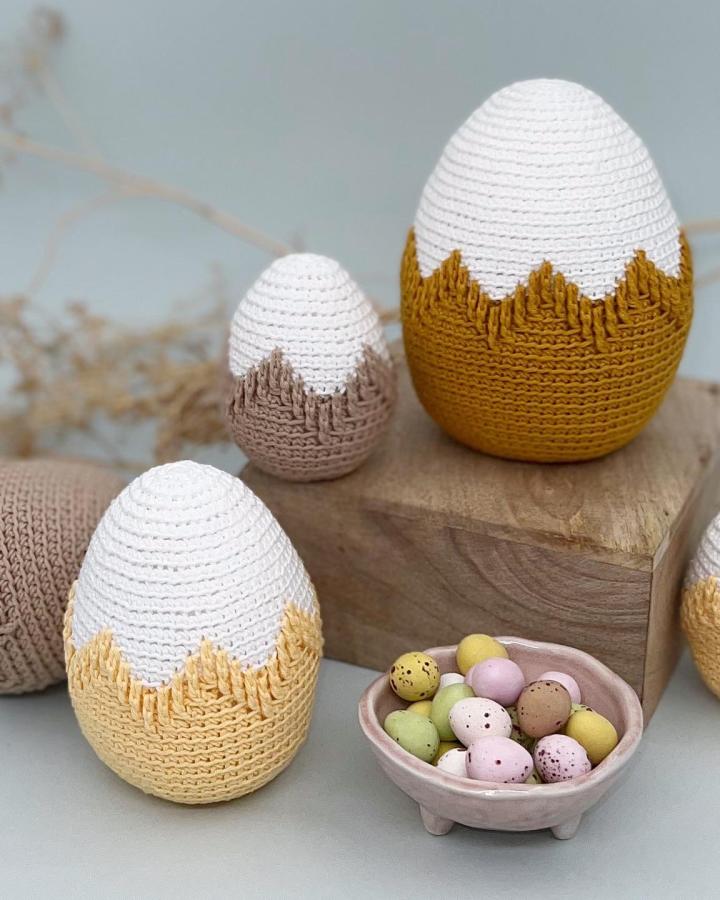 White and mustard jagged edge crochet eggs from @vibekemagnesen with pastel speckled candy eggs nearby for easter crochet ideas.