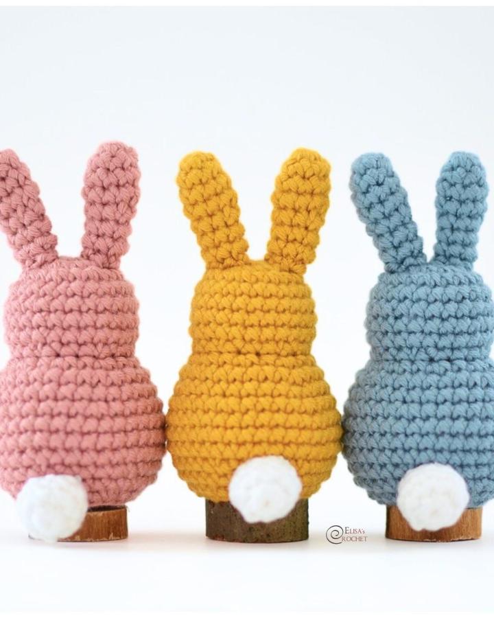 Pink, yellow, and blue chunky crochet bunnies with white tails on wooden bases from @littlebabyrorycrafts for easter crochet ideas.