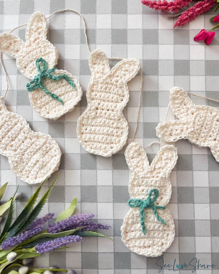 Cream-colored crochet bunny garland with green bows on checkered table from @thecrochetcounter perfect easter crochet ideas.