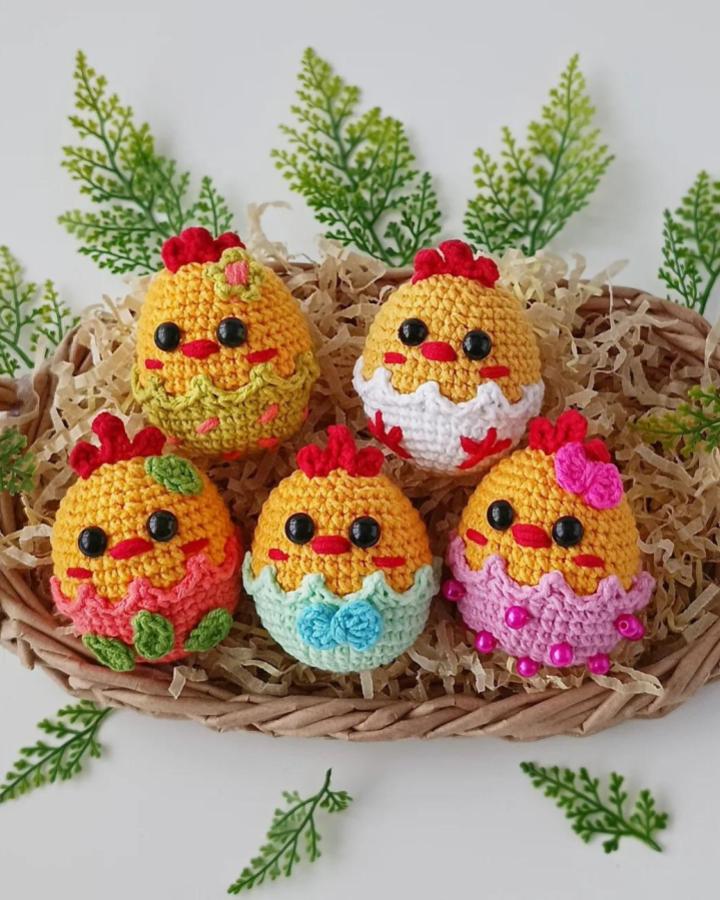 Yellow crochet chick eggs with colorful shells in a woven basket from @hookyarnandpaper surrounded by green leaves for easter crochet ideas.
