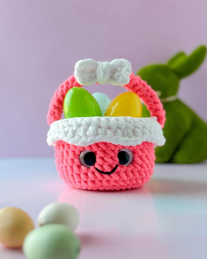 Coral pink and white mini crochet Easter basket from @elisascrochet filled with colorful plastic eggs and a cute bow.