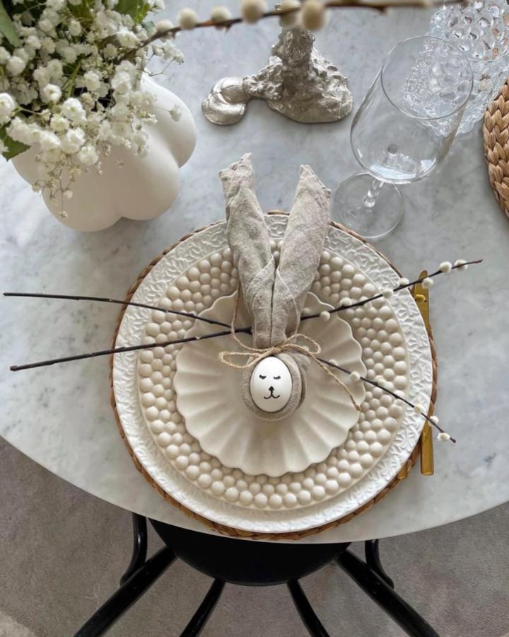 Neutral linen bunny napkin holder on textured white plates with woven charger and pussy willow branches from @insidetoo for easter table decor ideas