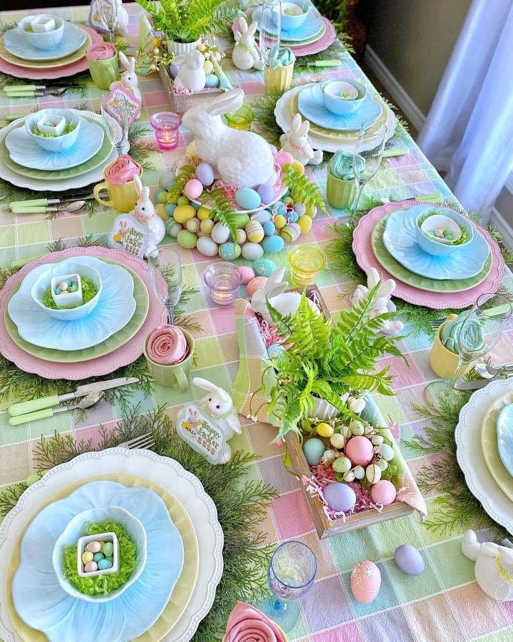 Pastel layered plates and ceramic bunnies on checkered tablecloth from @dining_delight with colorful Easter egg accents.