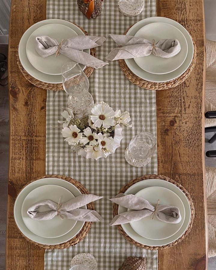 Soft green gingham table runner with woven chargers and neutral linens on rustic wooden table from @devonhomelife. Easter table decor ideas.