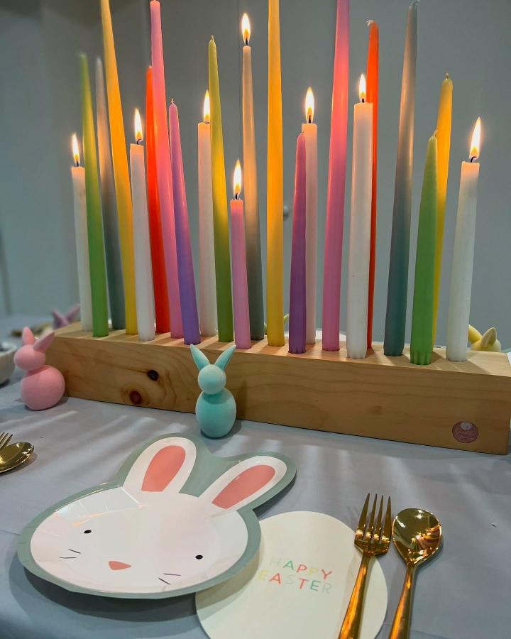 Colorful pastel tapered candles in a wooden holder from @candlelifeco. Easter table decor ideas with bunnies and gold utensils.
