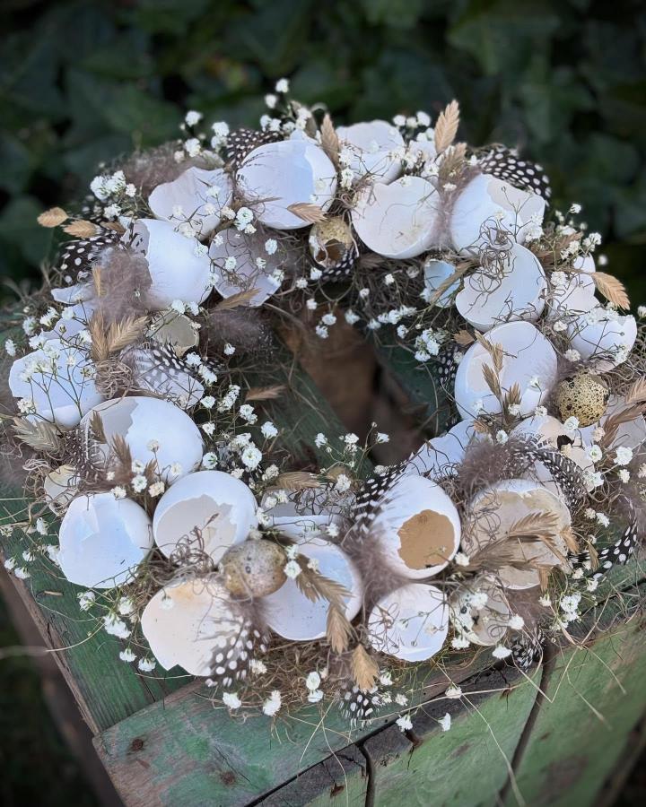 White and beige eggshell wreath with feathers and baby's breath from @fru.lily on rustic green wood surface for easter wreath ideas.