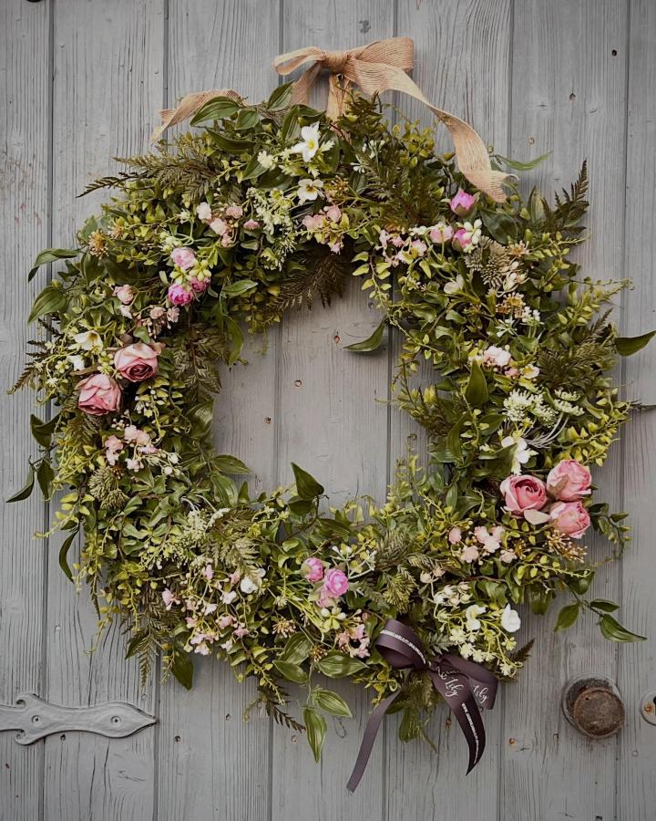 greenery and pink floral Easter wreath ideas from @jasmineandlilyfloralwreaths with rustic ribbons on wooden door
