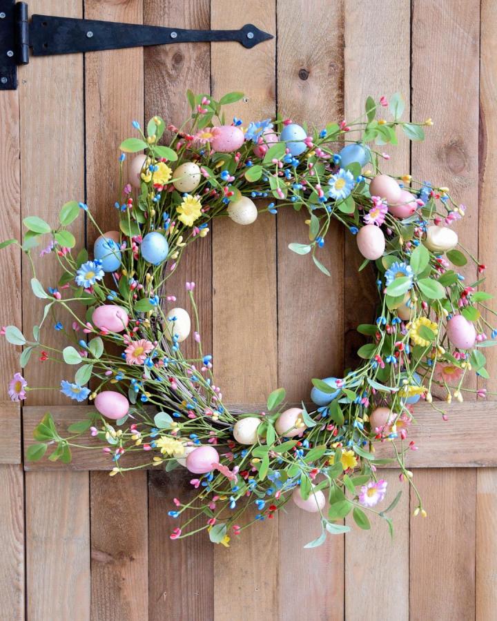 Pastel egg and floral wreath on wooden door from @gisela_graham showing soft easter wreath ideas with vibrant small flowers and greenery.