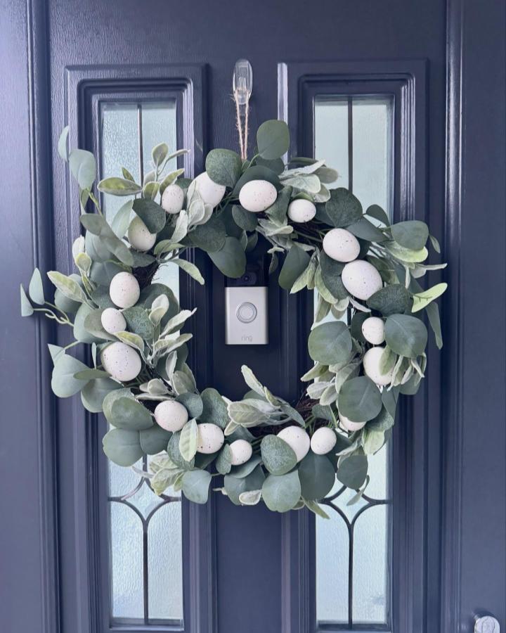 Green eucalyptus wreath with white speckled eggs hanging on a dark front door from @the_semi_by_the_sea. Simple, elegant Easter wreath ideas.