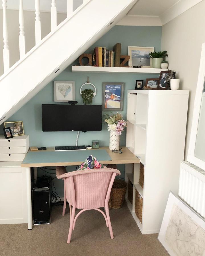 White Kallax desk setup with pastel pink chair and blue accent wall from @lovely.cuppa.tea under stairs ikea kallax desk hacks & ideas.