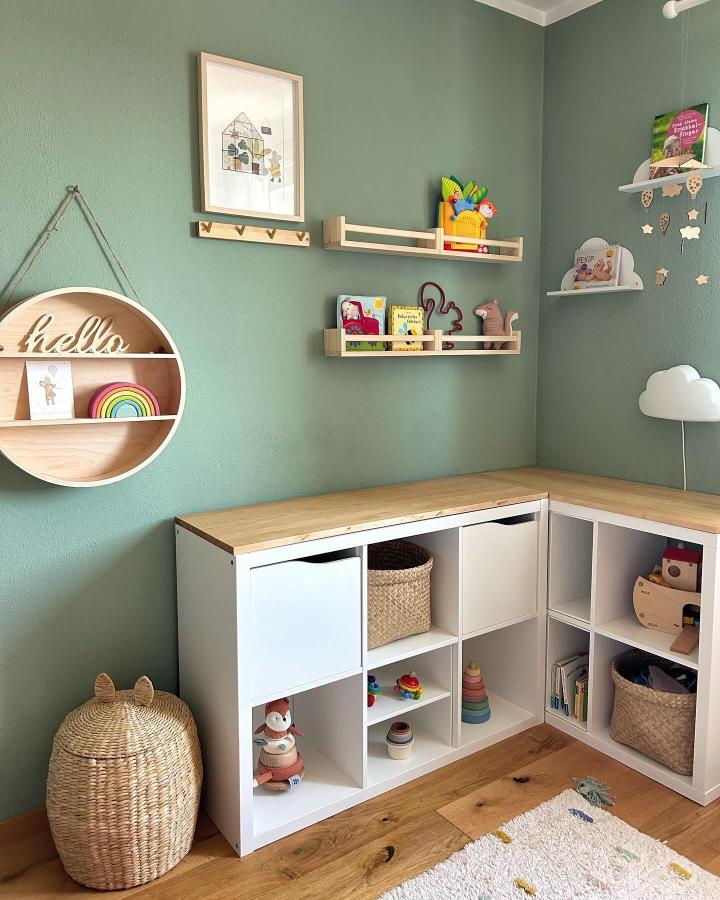 Light wood-topped white ikea kallax playroom hacks & ideas with woven baskets and sage green walls from @unserhausamwimhof. Cozy corner toy storage with shelves and hooks.