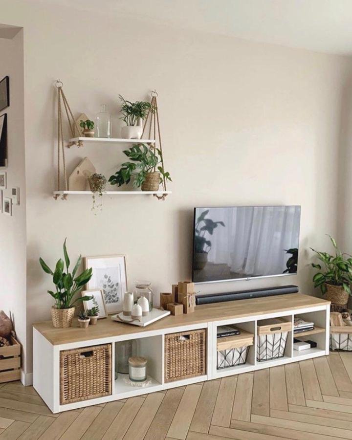 White and oak Ikea Kallax TV unit with woven baskets and green plants from @inspideco_21 in cozy living room setting.