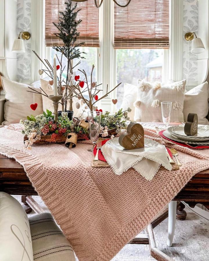 Pink chunky knit blanket on rustic wooden table with natural twig centerpiece and heart decorations from @silvanapapier valentines table decor ideas.