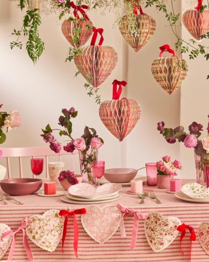Vintage paper honeycomb hearts hanging with red ribbons from @florisinaforest. Romantic valentines table decor ideas with soft florals and greenery.