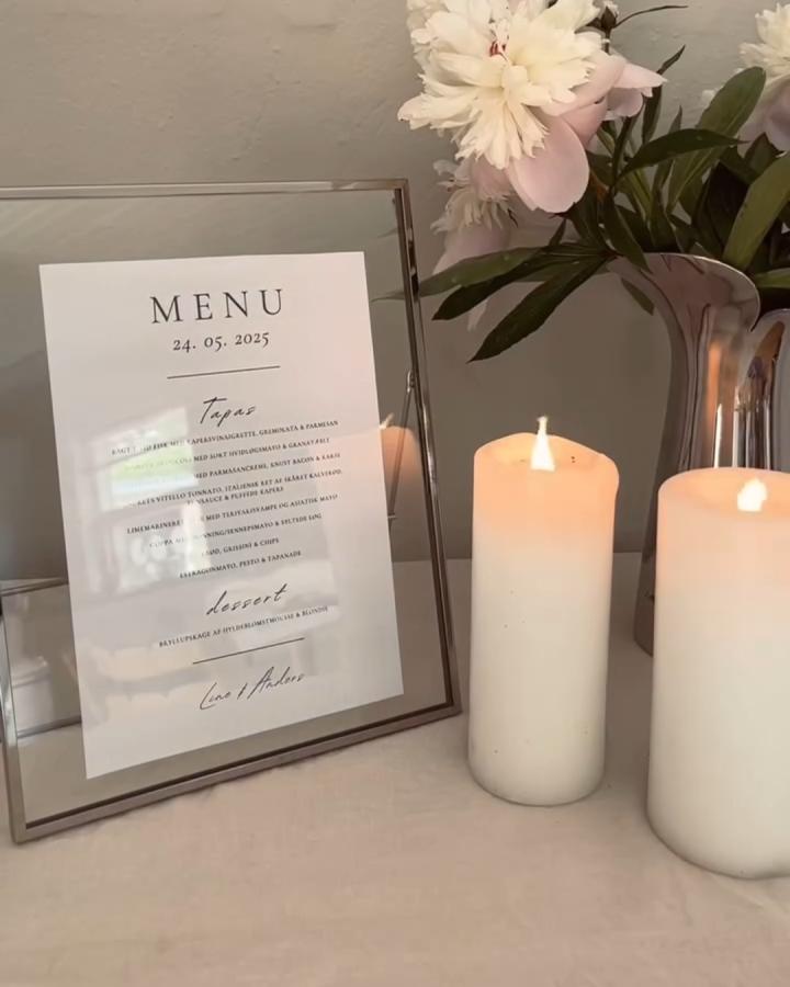 neutral-toned glass frame and candle wedding menu display from @linekohsel with a floral arrangement in the background