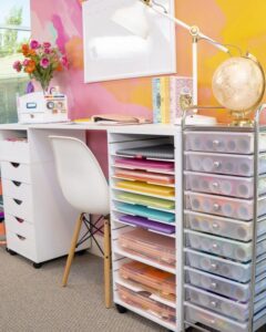 white and clear craft room with rolling storage units on wheels from Happiness Is Homemade. Rainbow paper stacks and transparent drawers keep supplies tidy