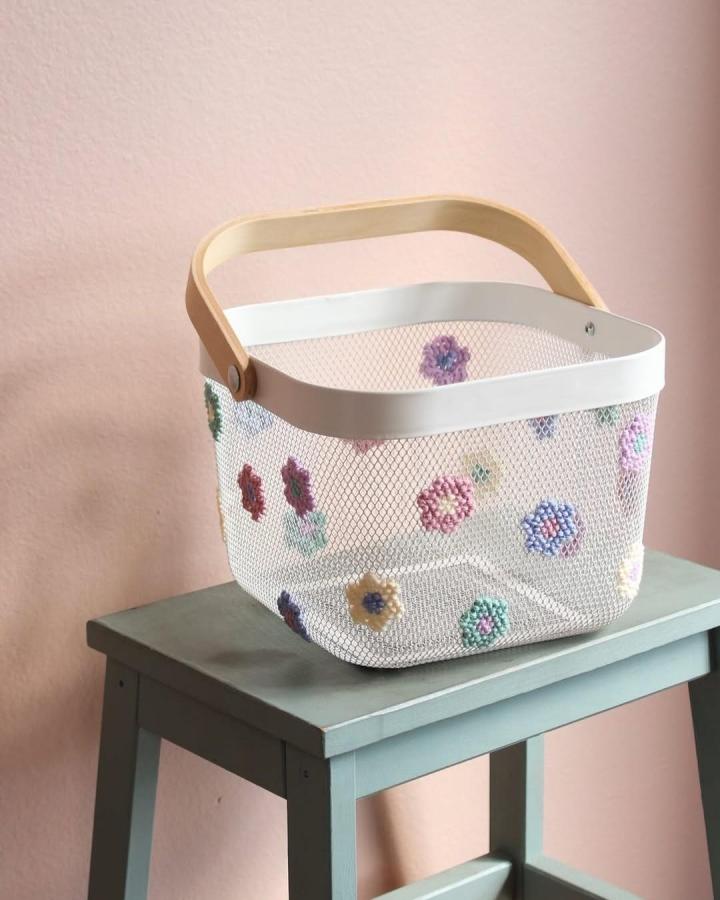 White mesh Ikea Risatorp basket decorated with multicolored crochet flowers on a teal stool from @entertainidea for easter basket ideas.