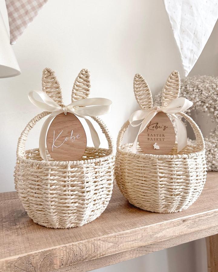 Cream woven bunny ear baskets with satin ribbons from @lovemagentashop. Personalized wooden egg tags decorate charming easter basket ideas.