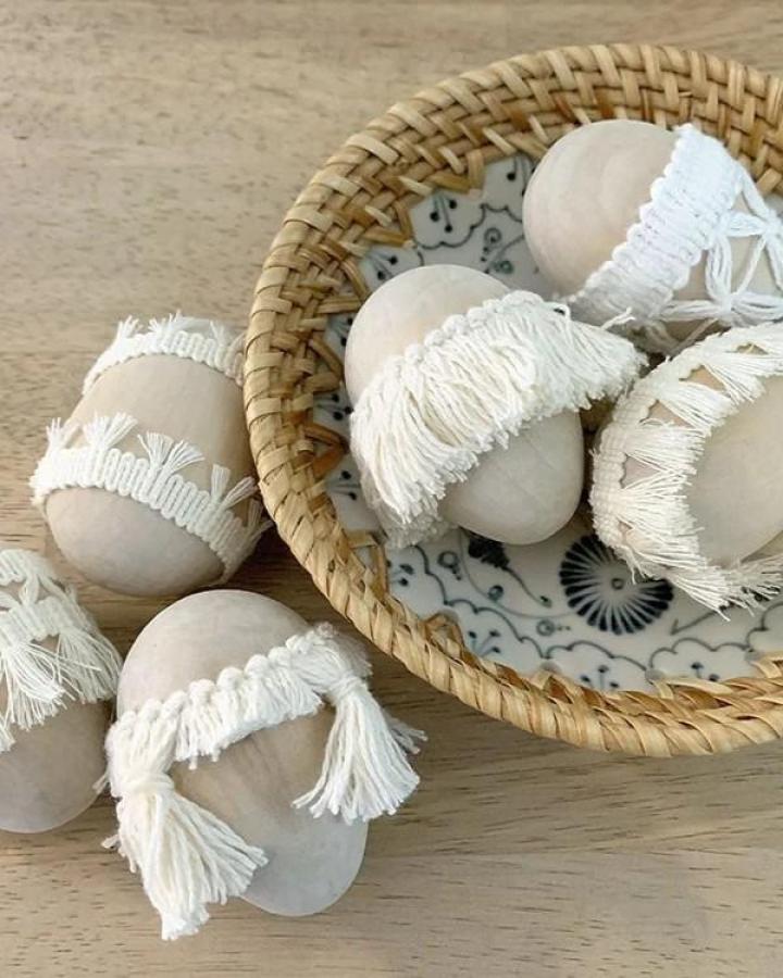 neutral boho tassel Easter egg decorating ideas for adults wooden eggs in wicker bowl with cream cotton fringe